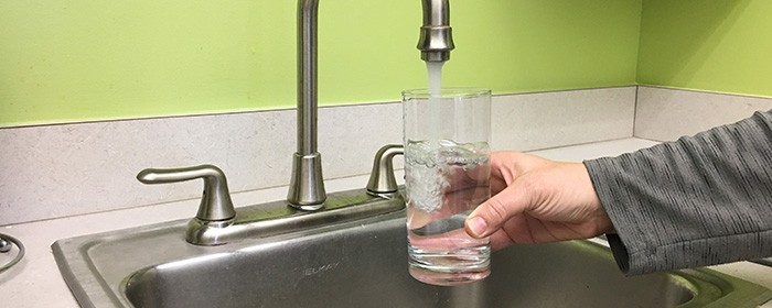 water flowing from faucet into a glass held by a hand